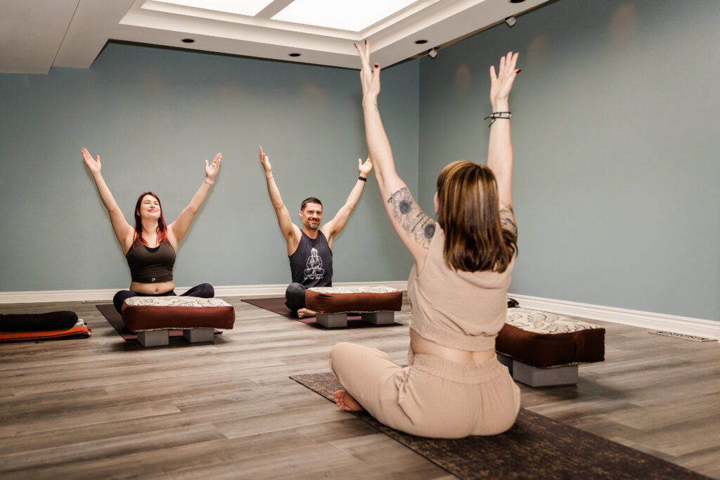 A woman yoga instructor and two students with hands in the air during a yoga session.